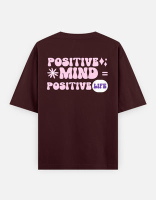 Oversized t-shirt with pastel pink retro typography reading “Positive Mind = Positive Life,” decorated with flower and sparkle icons for a motivational vibe.