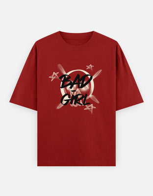Oversized t-shirt with bold graffiti text “Bad Girl” over a skull-and-crossbones graphic, accented with stars for an edgy streetwear look.