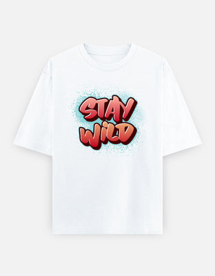 Oversized graffiti-style t-shirt with bold red-orange lettering “Stay Wild” over a turquoise spray-paint splatter background.