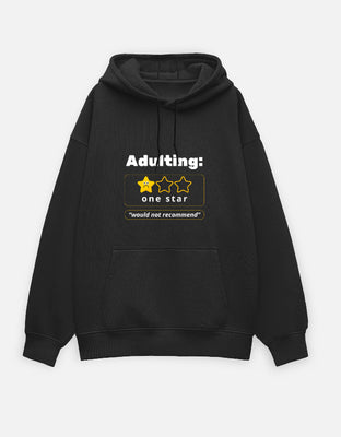 Oversized black hoodie with a review-style graphic reading “Adulting: one star — would not recommend” and a 1 out of 3 star rating.