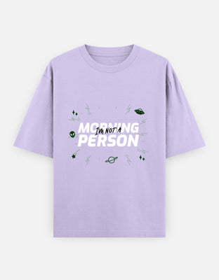 Oversized t-shirt with bold white typography reading “Morning Person” with “Not” scribbled across, surrounded by doodles of aliens, UFOs, stars, and zaps in green.